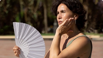 Older woman fanning herself and looking flushed, indicating a hot flash.