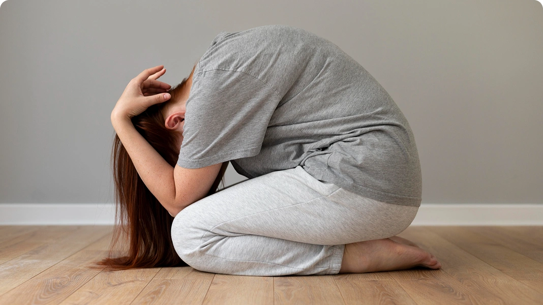 Person kneeling on the floor with head in hands, depicted with dark smoke rising from their head, symbolizing mental distress.