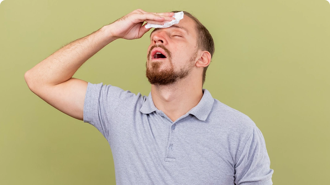 Man sweating heavily and wiping his forehead with a tissue.